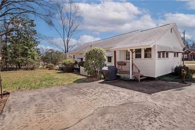 view of front of property featuring a wooden deck, concrete driveway, a front lawn, and a shingled roof