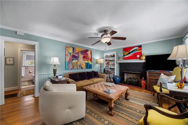 living area featuring a brick fireplace, wood finished floors, a wainscoted wall, and a textured ceiling