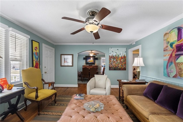 living area with arched walkways, crown molding, baseboards, and wood finished floors