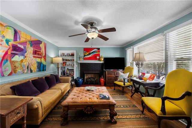 living area with wood finished floors, a fireplace, ornamental molding, ceiling fan, and a textured ceiling