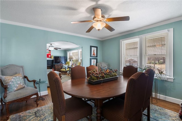 dining area featuring arched walkways, ornamental molding, a textured ceiling, and wood finished floors