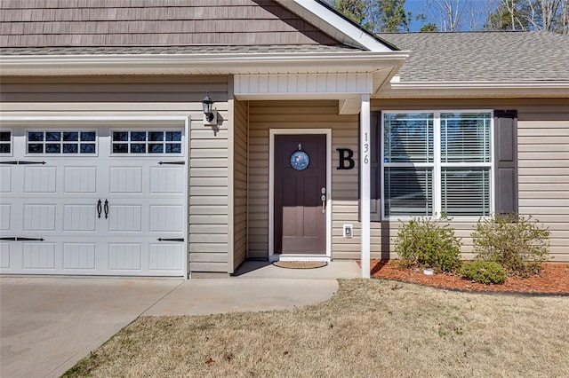 entrance to property featuring a garage, roof with shingles, and concrete driveway