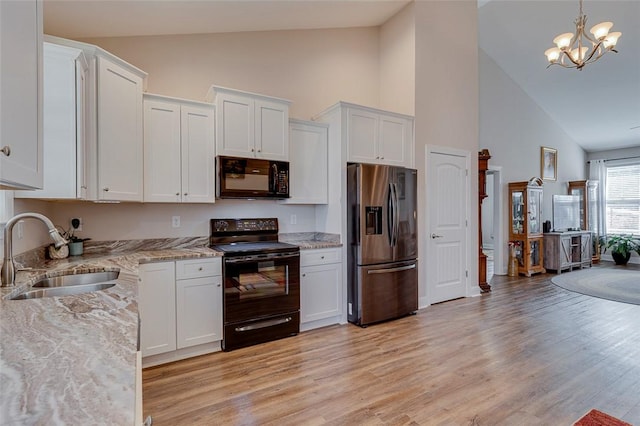 kitchen with light stone countertops, light wood-type flooring, white cabinets, black appliances, and a sink