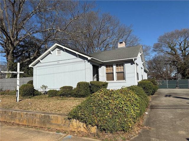 view of property exterior with brick siding, a shingled roof, fence, a chimney, and driveway