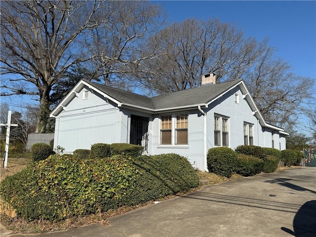 view of property exterior featuring brick siding, fence, roof with shingles, a chimney, and an attached garage