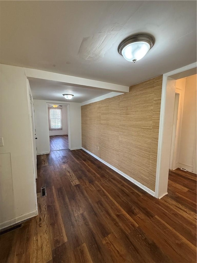 unfurnished room with beamed ceiling, dark wood-style floors, visible vents, and baseboards