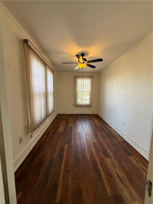 empty room featuring baseboards, dark wood-style floors, a ceiling fan, and crown molding