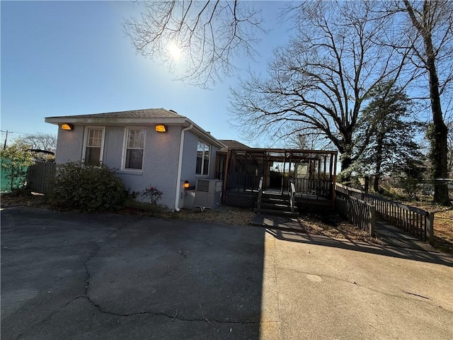 view of front of house with brick siding, a deck, and fence