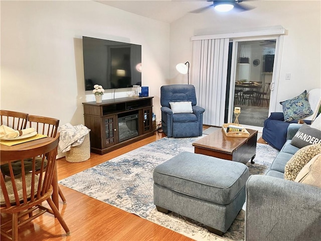 living room featuring a glass covered fireplace, wood finished floors, and a ceiling fan