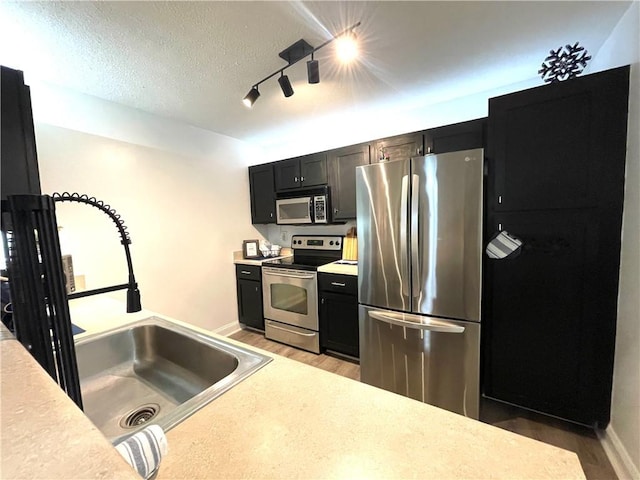 kitchen featuring baseboards, light wood-type flooring, light countertops, stainless steel appliances, and a sink