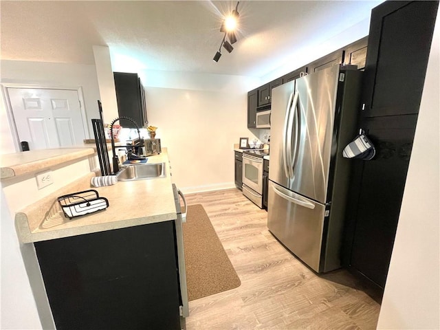 kitchen featuring light wood finished floors, baseboards, light countertops, stainless steel appliances, and a sink