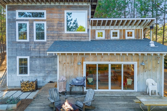 rear view of property with a fire pit, a deck, and a shingled roof