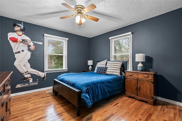 bedroom featuring multiple windows, baseboards, light wood-type flooring, and a textured ceiling