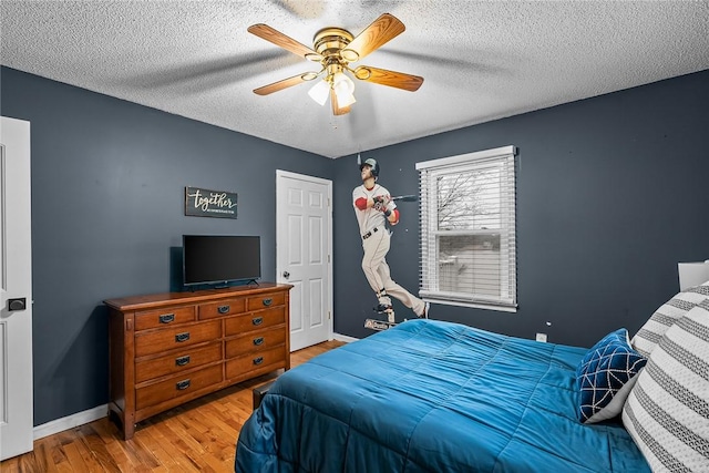 bedroom with ceiling fan, baseboards, a textured ceiling, and wood finished floors