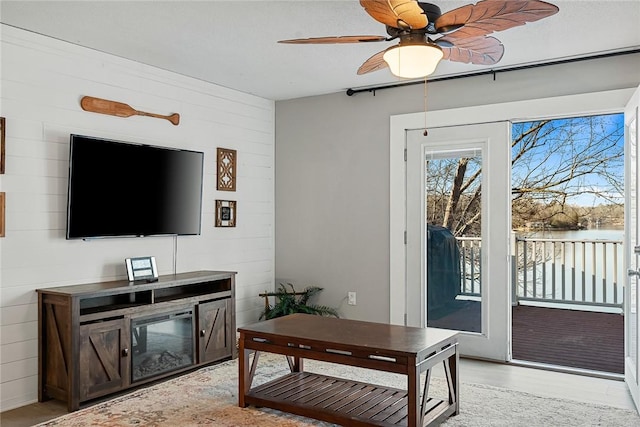 living area featuring wooden walls, light wood-style flooring, and ceiling fan