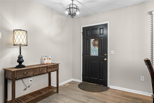 foyer with light wood finished floors, visible vents, a chandelier, and baseboards