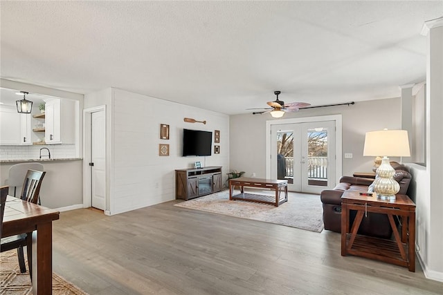 living area featuring light wood-style flooring, french doors, a textured ceiling, and ceiling fan