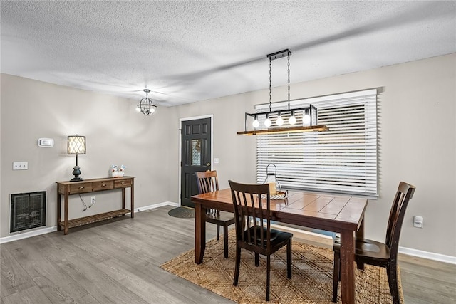 dining space with a textured ceiling, baseboards, and wood finished floors