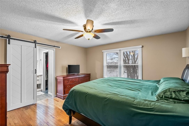 bedroom featuring a spacious closet, ceiling fan, light wood-type flooring, a barn door, and a textured ceiling