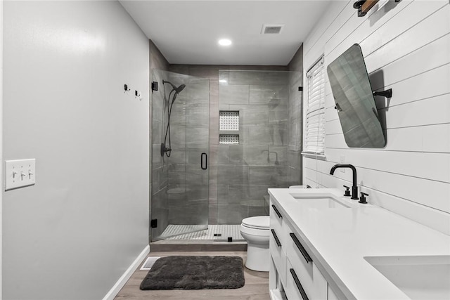 full bath featuring toilet, a stall shower, a sink, wood finished floors, and double vanity