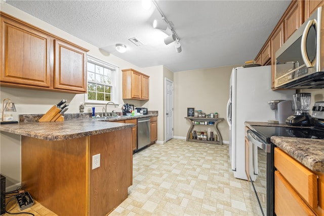 kitchen with a peninsula, a sink, appliances with stainless steel finishes, a textured ceiling, and dark countertops