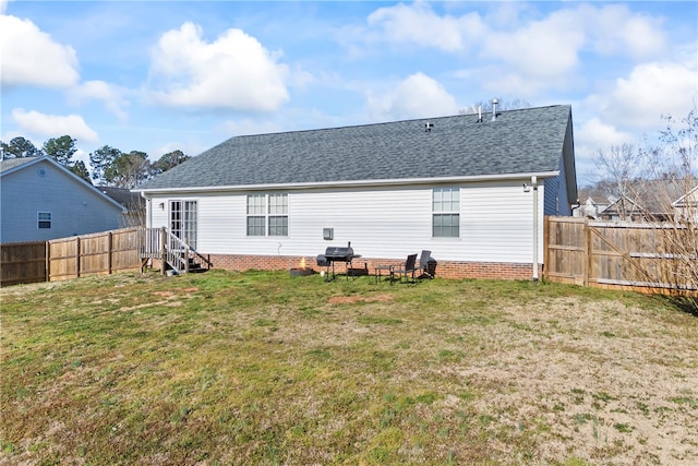 back of house with a fenced backyard, a lawn, and roof with shingles