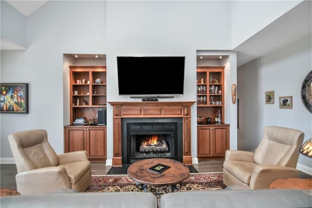 living area featuring baseboards, a fireplace with flush hearth, a high ceiling, and wood finished floors