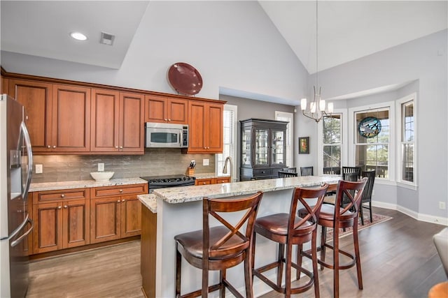 kitchen featuring brown cabinetry, backsplash, stainless steel appliances, and light stone counters