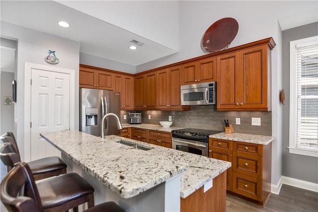 kitchen with visible vents, a sink, appliances with stainless steel finishes, brown cabinetry, and decorative backsplash