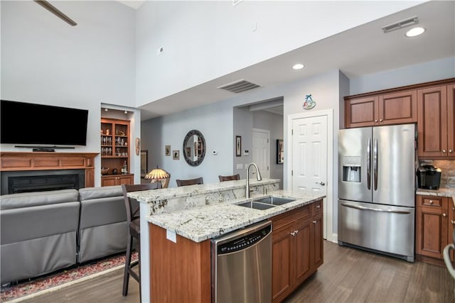 kitchen featuring open floor plan, light stone counters, wood finished floors, stainless steel appliances, and a sink