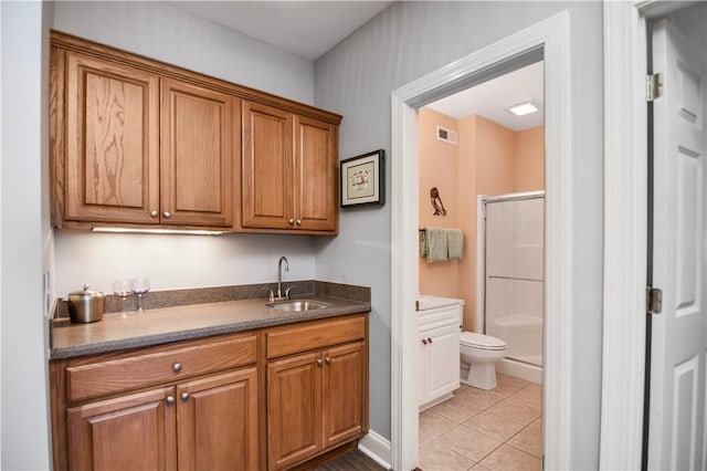 kitchen featuring visible vents, brown cabinets, a sink, dark countertops, and light tile patterned floors