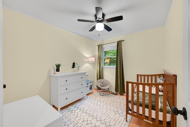 bedroom with a crib, light wood-type flooring, and ceiling fan