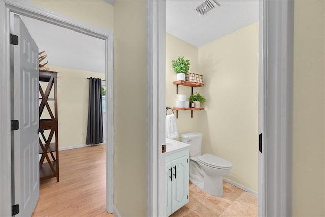 bathroom featuring visible vents, baseboards, toilet, wood finished floors, and vanity