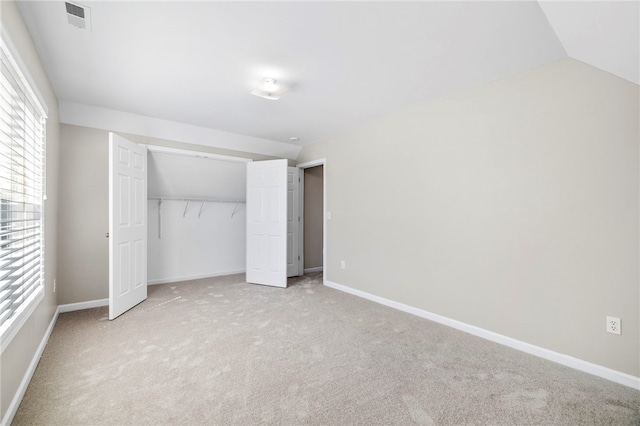 unfurnished bedroom with light carpet, visible vents, baseboards, and lofted ceiling