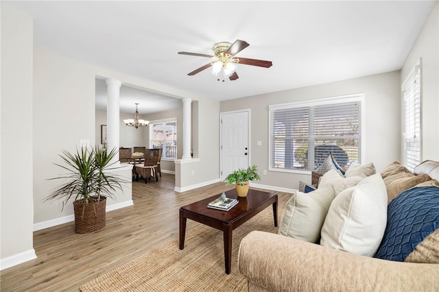 living area with light wood-type flooring, decorative columns, baseboards, and ceiling fan with notable chandelier