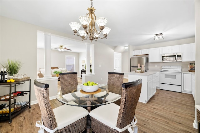 dining room with light wood finished floors, ceiling fan with notable chandelier, baseboards, and ornate columns