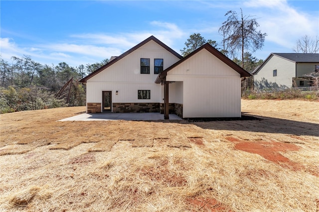 rear view of house featuring stone siding and a patio