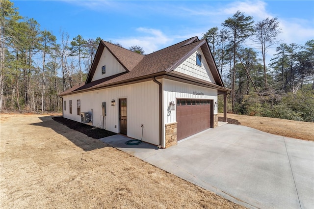 view of home's exterior with stone siding, an attached garage, concrete driveway, and roof with shingles