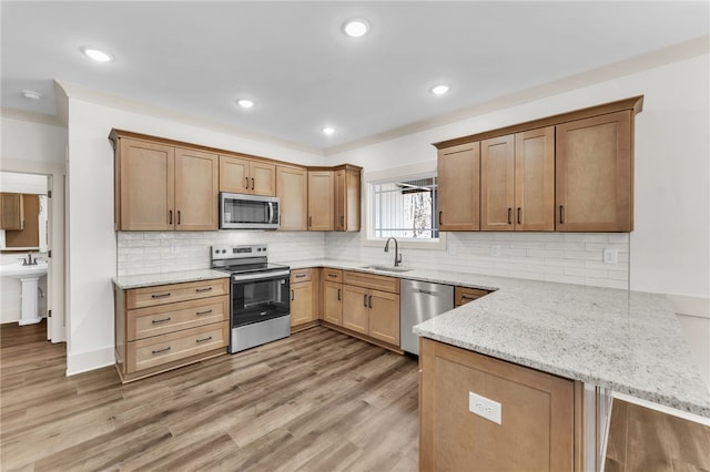 kitchen featuring a sink, stainless steel appliances, a peninsula, light wood finished floors, and light stone countertops