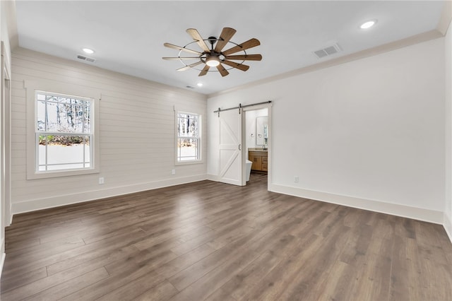 empty room with a barn door, visible vents, dark wood finished floors, and a ceiling fan