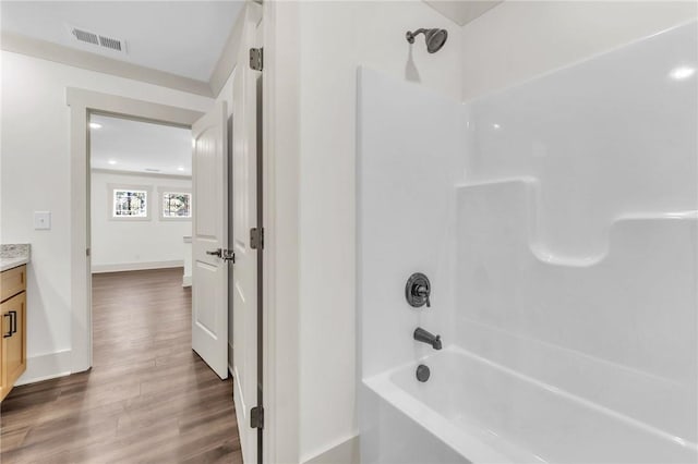 bathroom with visible vents, shower / tub combination, wood finished floors, baseboards, and vanity