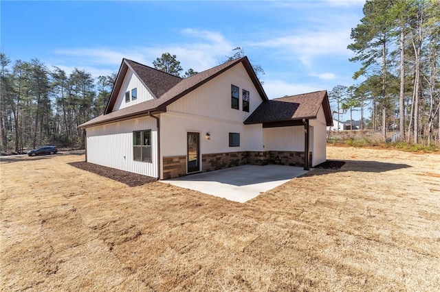 rear view of property with a patio area, stone siding, and a shingled roof