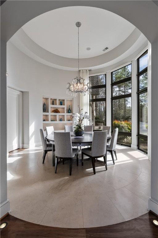 dining space featuring a raised ceiling, arched walkways, a chandelier, and a towering ceiling