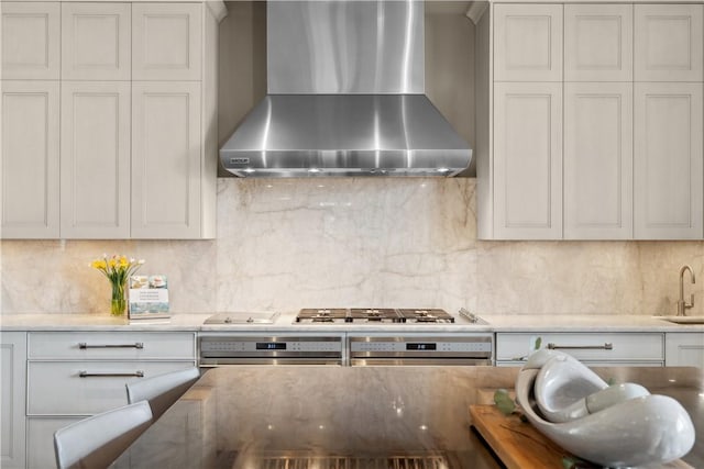 kitchen with oven, backsplash, stainless steel gas stovetop, and wall chimney range hood