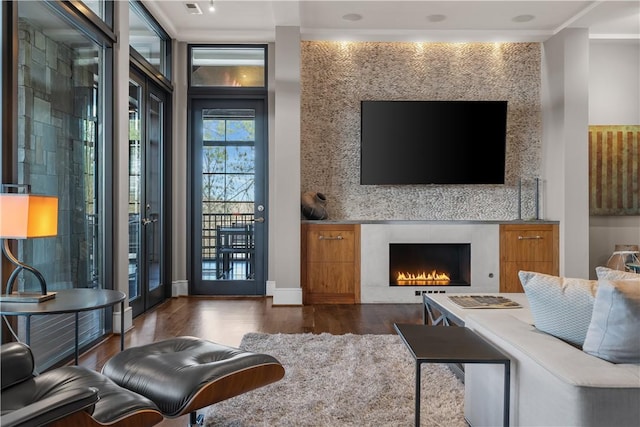 living area featuring wood finished floors, baseboards, french doors, and a lit fireplace