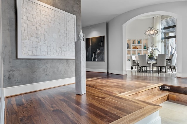 interior space featuring baseboards, wood finished floors, arched walkways, and a chandelier