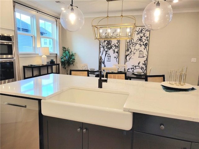 kitchen with decorative light fixtures, ornamental molding, light stone counters, stainless steel appliances, and a sink