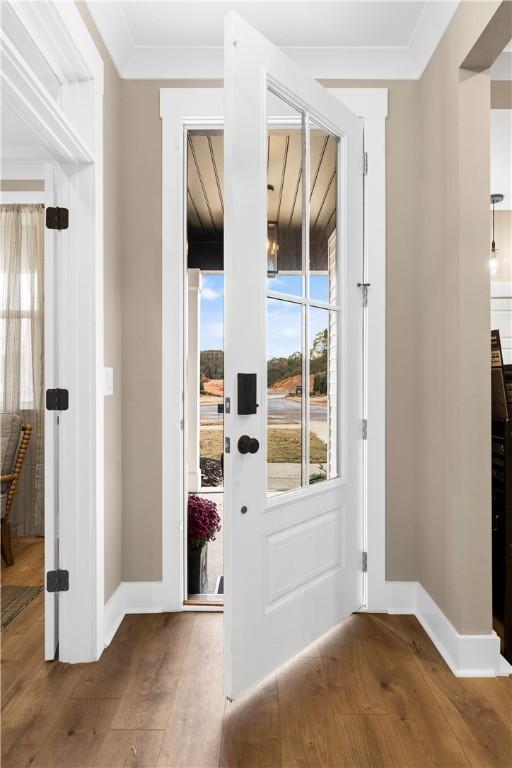 doorway to outside with wood finished floors, baseboards, and ornamental molding