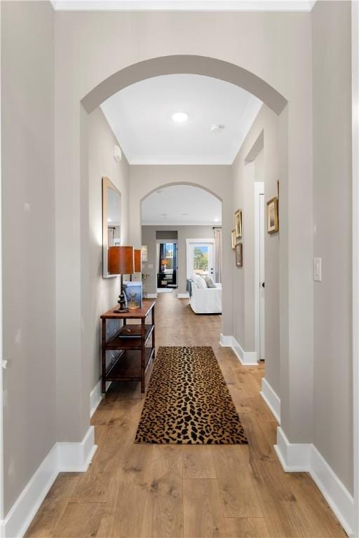 corridor with baseboards, arched walkways, and light wood-style flooring