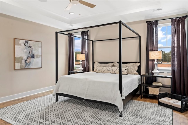 bedroom featuring a ceiling fan, wood finished floors, baseboards, visible vents, and a raised ceiling